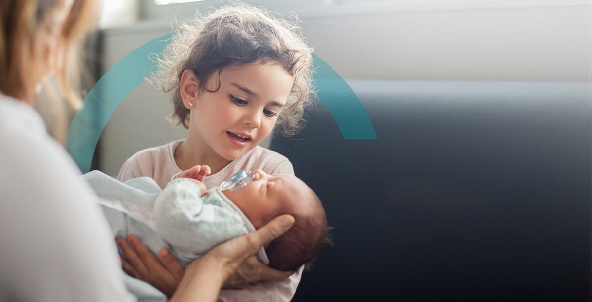 Nurse shows newborn baby to older sister in hospital enviroment