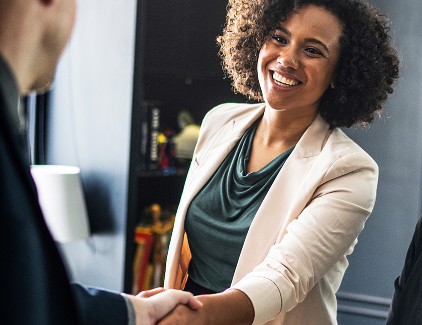 Man and woman smiling and shaking hands in business setting